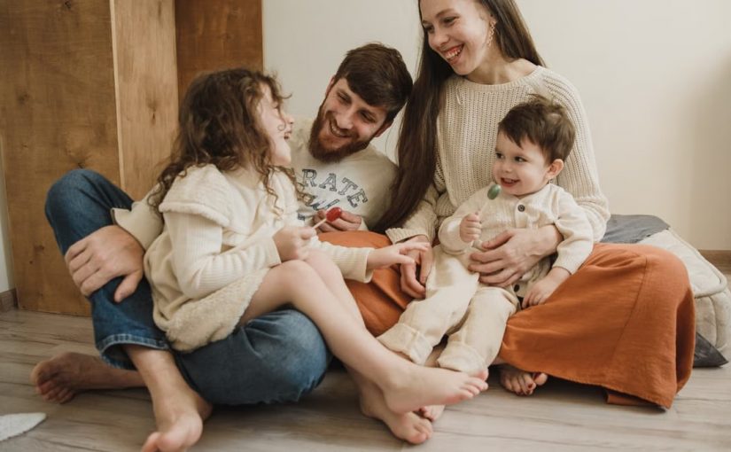 Smiling family of four sitting on the living room floor, enjoying quality time together.